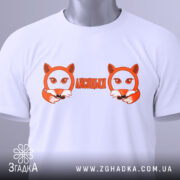 Футболка лисицьки білого кольору, складена на поверхні, з видимим етикеткою, фон світлий, принт з двома лисицями та написом 'ЛИСИЦЬКИ' оранжевого кольору.