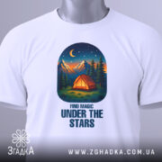 Футболка магія нічного лісу, біла, зображена зверху, на фоні світло-сірого градієнта, принт з малюнком намету, гір та зірок на нічному небі, з етикеткою на рукаві.