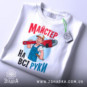 Футболка майстер на всі руки, біла, зображена в складеному вигляді, фон світло-сірий, принт з майстром, який тримає червоний ключ, текст яскравий, червоний і блакитний, на футболці є етикетка з логотипом.