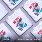 Футболка майстер на всі руки, біла, зображена з фронтального ракурсу на манекені, фон світло-сірий, принт з веселим майстром, який тримає червоний ключ, текст на футболці яскравий, червоний і блакитний.