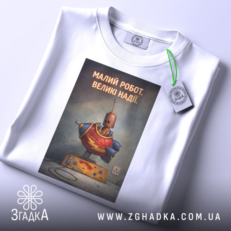 Футболка малий робот надії білого кольору, зображена зверху, на ній підвішений ярлик, фон світлий, принт з малюнком робота в червоному костюмі з написом 'МАЛИЙ РОБОТ. ВЕЛИКІ НАДІЇ.'