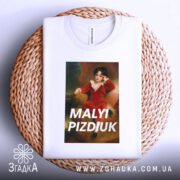 Футболка малий шибеник, біла, складена на плетеному кошику, фон світло-блакитний, принт з портретом хлопчика в червоному костюмі, текст 'MALYI PIZDIUK' великими літерами.