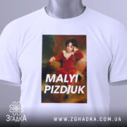Футболка малий шибеник, біла, складена на столі, фон світло-блакитний, принт з портретом хлопчика в червоному костюмі, текст 'MALYI PIZDIUK' великими літерами, на футболці є етикетка з зеленим шнурком.