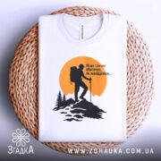 Футболка мандрівки надихають. Біла футболка, складена на плетеній основі, з принтом альпініста на фоні жовтого сонця. Принт чорного кольору, деталі лісу та гір добре проглядаються, футболка виглядає привабливо.