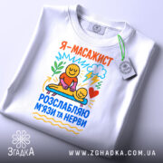 Футболка масажист білого кольору, зображена зверху, фон світлий, принт яскравий з малюнками усміхнених персонажів, які виконують масаж, текст на футболці українською мовою, на комірці є етикетка.