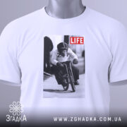 Футболка мавпа на велосипеді, біла, складена на поверхні, фон світлий, принт зображає мавпу на велосипеді з написом 'LIFE', на футболці є етикетка.