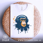 Футболка мавпа в навушниках, біла, зображена на плетеній кошику зверху, фон світло-сірий, принт зображає мавпу в навушниках з кольоровими плямами та метеликами.