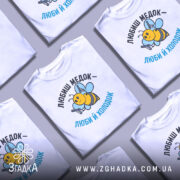 Футболка медок холодок, біла, зображена на манекені, фон світло-сірий, принт з бджолою, яка тримає пістолети, текст чорного та блакитного кольору.