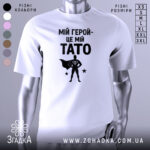 Футболка мій герой тато, біла, зображена на манекені, фон світло-сірий, принт чорний з написом 'МІЙ ГЕРОЙ-ЦЕ МІЙ TATO' та силуетом супергероя.