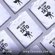 Футболка мій герой тато, біла, зображена на манекені, фон світло-сірий, принт чорний з написом 'МІЙ ГЕРОЙ-ЦЕ МІЙ TATO' та силуетом супергероя.