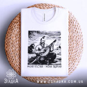 Футболка моя пісня зброя, складена біла футболка на плетеній основі, ракурс зверху, фон світло-сірий, принт з кобзарем, який грає на бандурі, з написом 'Моя пісня - моя зброя'.