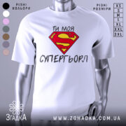 Футболка моя супергьорл, біла, зображена з фронтального ракурсу, фон світло-сірий, принт з червоним логотипом Супермена та текстом "ТИ МОЯ СУПЕРГЬОРЛ" чорного кольору.