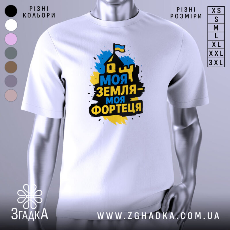 Футболка моя земля фортеця, біла, зображена на манекені з правого боку, фон світло-сірий, принт з написом 'Моя земля - моя фортеця' у жовто-синіх кольорах з зображенням будинку та прапора.