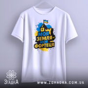 Футболка моя земля фортеця, біла, зображена на манекені з лівого боку, фон світло-сірий, принт з написом 'Моя земля - моя фортеця' у жовто-синіх кольорах з зображенням будинку та прапора.
