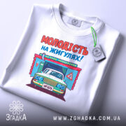 Футболка молодість на жигулях, біла, складена на столі, фон світло-сірий, принт з автомобілем та написом 'МОЛОДІСТЬ НА ЖИГУЛЯХ!' яскравий, з елементами дизайну.