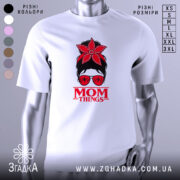 Футболка Mom Thing, білого кольору, зображена з близького ракурсу, на фоні градієнтного сірого кольору, принт з червоною квіткою на голові жінки в окулярах та написом 'MOM THINGS' під малюнком.