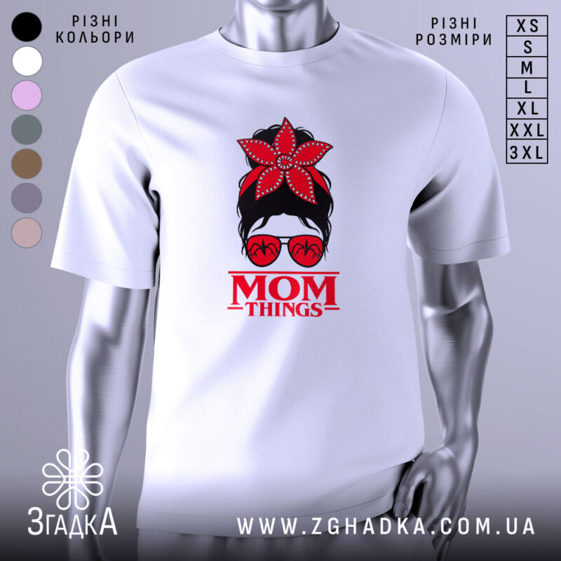 Футболка Mom Thing, білого кольору, зображена з близького ракурсу, на фоні градієнтного сірого кольору, принт з червоною квіткою на голові жінки в окулярах та написом 'MOM THINGS' під малюнком.