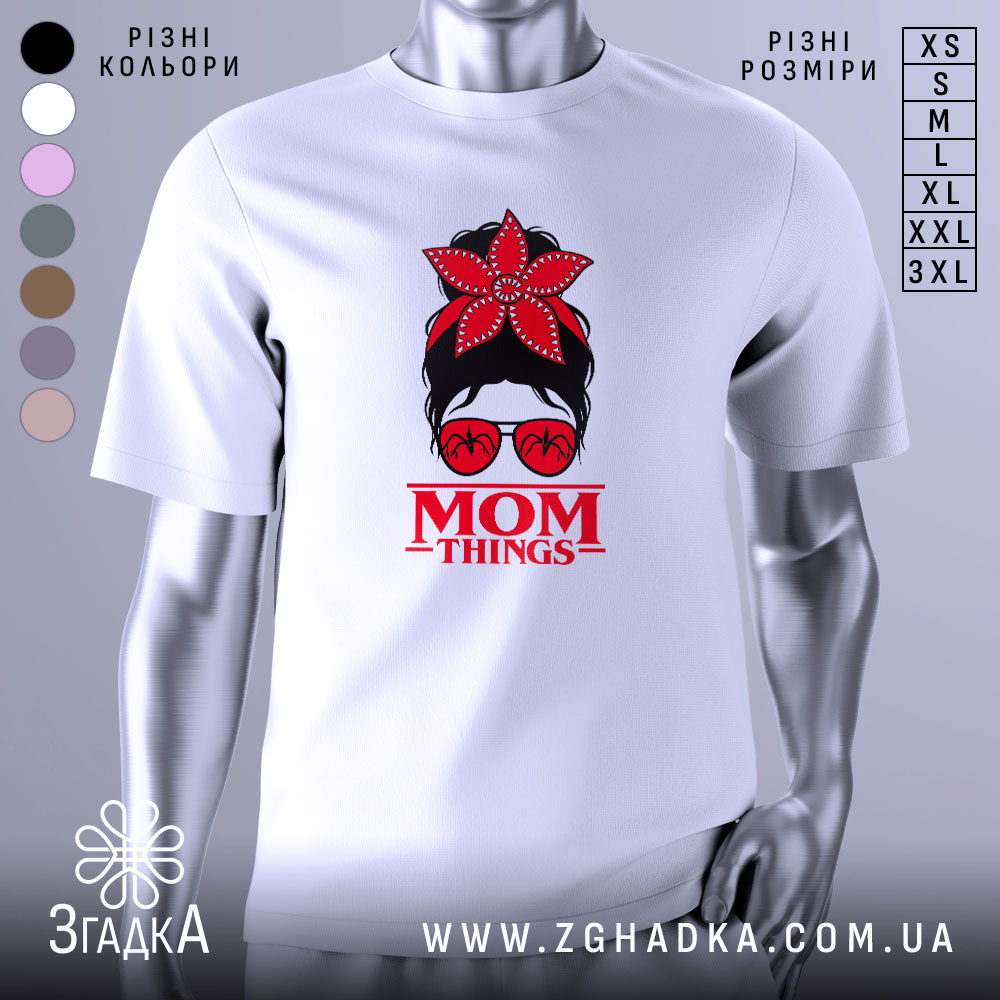 Футболка Mom Thing, білого кольору, зображена з близького ракурсу, на фоні градієнтного сірого кольору, принт з червоною квіткою на голові жінки в окулярах та написом 'MOM THINGS' під малюнком.