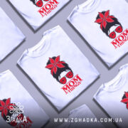 Футболка Mom Thing, білого кольору, зображена з близького ракурсу, на фоні градієнтного сірого кольору, принт з червоною квіткою на голові жінки в окулярах та написом 'MOM THINGS' під малюнком.