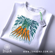 Футболка морква арт, біла, складена на поверхні, фон світло-сірий, принт зображує три помаранчеві морквини з зеленим листям, на комірці є етикетка.