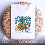 Футболка морква арт, біла, складена на плетеній кошику, фон білий, принт зображує три помаранчеві морквини з зеленим листям.