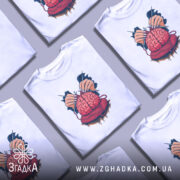 Футболка мозок в клубку, біла, зображена з фронтального ракурсу, на нейтральному фоні, принт з червоним мозком, що оточений руками з голками та клубком червоної пряжі.