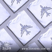 Футболка мрія не вмирає, біла, зображена на манекені, фон світло-сірий, принт з літаком та написом 'МРІЯ НІКОЛИ НЕ ВМИРАЄ' у чорному кольорі з жовтим сердечком.