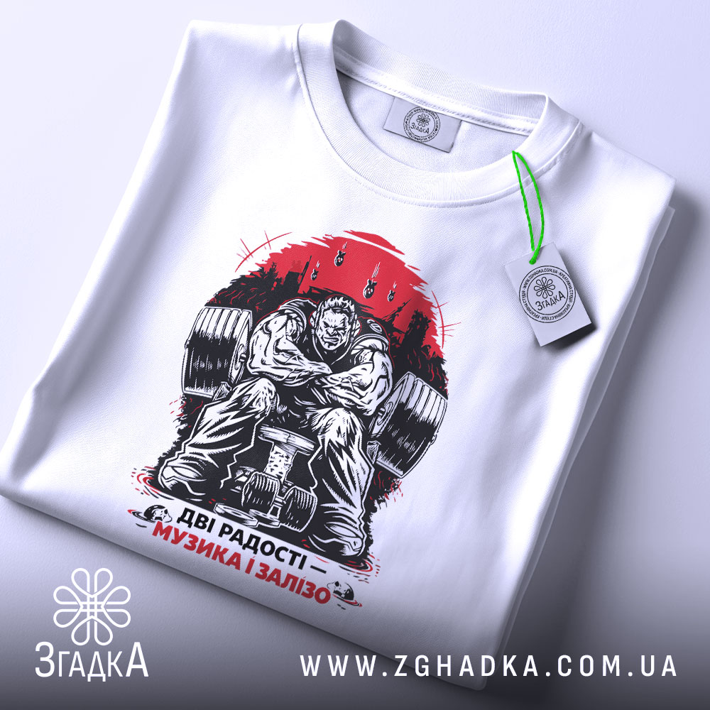 Футболка музика і залізо, біла, складена на столі, фон світлий, принт зображає м'язистого чоловіка на тренажері, червоний фон з написом 'ДВІ РАДОСТІ – МУЗИКА І ЗАЛІЗО', на комірці є етикетка.