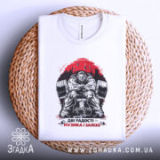 Футболка музика і залізо, біла, складена на плетеному кошику, фон світлий, принт зображає м'язистого чоловіка на тренажері, червоний фон з написом 'ДВІ РАДОСТІ – МУЗИКА І ЗАЛІЗО'.