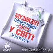 Футболка музикант білого кольору, зображена в плоскому вигляді, з принтом червоного та синього кольорів, текст розташований по центру, на комірці видна етикетка, фон світло-сірий.