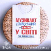 Футболка музикант білого кольору, зображена в плоскому вигляді на плетеній основі, з принтом червоного та синього кольорів, текст розташований по центру, фон світло-сірий.