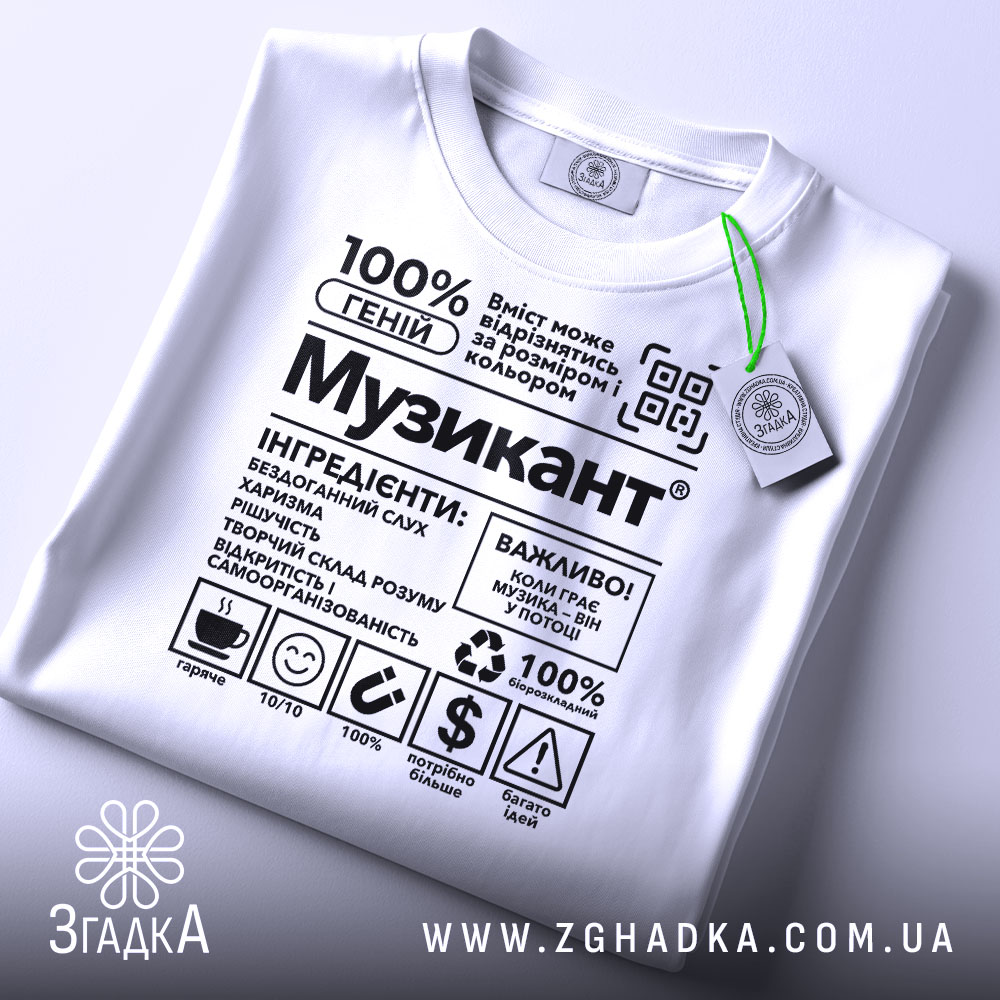 Футболка музикант білого кольору, складена на поверхні, з принтом у чорному кольорі, на фоні світло-сірого кольору, з зеленим ярликом, що звисає з коміра.