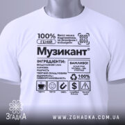Футболка музикант білого кольору, складена на поверхні, з принтом у чорному кольорі, на фоні світло-сірого кольору, з зеленим ярликом, що звисає з коміра.
