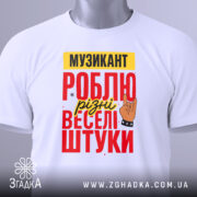 Футболка музикант білого кольору, складена на поверхні, фон світлий, принт з текстом "МУЗИКАНТ РОБЛЮ різні веселі штуки" в червоному, жовтому та чорному кольорах, з малюнком руки в жесті рок-знака, на футболці є етикетка.