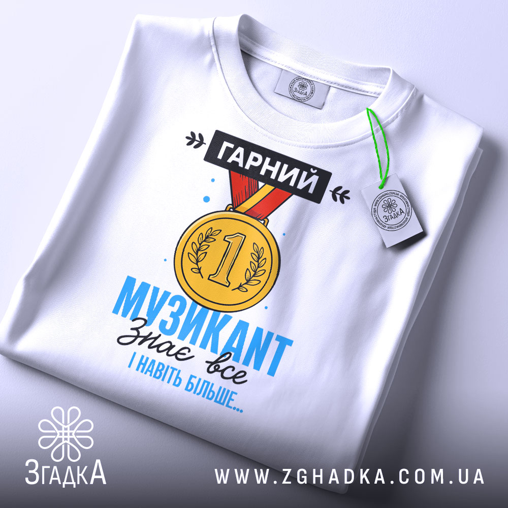 Футболка музикант, біла, зображена зверху, на ній підвішена етикетка, фон світло-сірий, принт з медаллю та текстом "ГАРНИЙ МУЗИКАНТ знає все І навіть більше..." у яскравих кольорах.