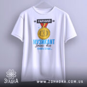 Футболка музикант, біла, зображена на вішалці, фон світло-сірий, принт з медаллю та текстом "ГАРНИЙ МУЗИКАНТ знає все І навіть більше..." у яскравих кольорах.