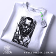 Футболка мисливець на морок, біла, лежить на поверхні, фон світло-сірий, принт чорного кольору з зображенням чоловіка в окулярах, з мечем і черепом, з етикеткою зеленого кольору.