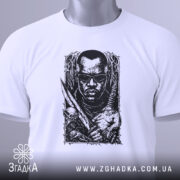 Футболка мисливець на морок, біла, лежить на поверхні, фон світло-сірий, принт чорного кольору з зображенням чоловіка в окулярах, з мечем і черепом, з етикеткою зеленого кольору.