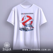Футболка мисливці за привидами, біла, показана з фронтального ракурсу, підвішена на вішалці, фон світло-сірий, принт з зображенням привида та автомобіля з фільму, з написом 'GHOSTRUSTERS'.