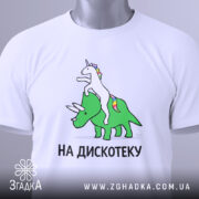 Футболка на дискотеку, біла, зображена на столі з легким нахилом, фон світло-сірий, принт з єдинорогом на трицератопсі, текст "НА ДИСКОТЕКУ" чорним шрифтом, видно етикетку.