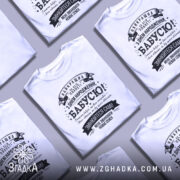 Футболка найкраща бабуся планети, біла, зображена з фронтального ракурсу, на нейтральному фоні, принт чорного кольору з текстом на українській мові та декоративними елементами.