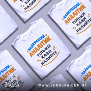 Футболка найкращий аналітик, білого кольору, зображена на манекені, фон світло-сірий, принт містить текст синього та оранжевого кольорів, з малюнками кавових зерен.