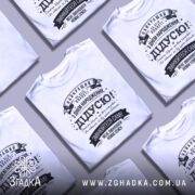 Футболка найкращий дідусь планети, біла, зображена на манекені, фон нейтральний, принт чорного кольору з текстом на українській мові, оформлений у стилі ретро з декоративними елементами.