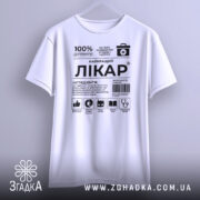 Футболка найкращий лікар, біла, підвішена на вішалці, фон світло-сірий, принт чорного кольору з медичними символами та текстом.