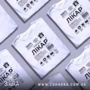 Футболка найкращий лікар, біла, зображена на манекені з правого боку, фон світло-сірий, принт чорного кольору з медичними символами та текстом.