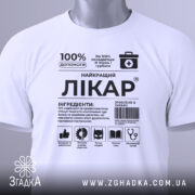Футболка найкращий лікар, біла, складена на столі, фон світло-сірий, принт чорного кольору з медичними символами, на комірці зелений ярлик.