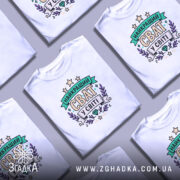 Футболка найкращий сват, біла, зображена з правого боку, на фоні світло-сірого кольору, принт з написом 'НАЙКРАЩИЙ СВАТ У СВІТІ' в кольорах зеленого, фіолетового та жовтого, оточений зірками та рослинними елементами.