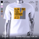 Футболка найкращий тракторист. Біла футболка з коротким рукавом, зображена з фронтального ракурсу. На фоні світло-сірий колір. Принт містить жовті та чорні елементи, з написом 'Найкращий тракторист' та зображеннями тракторів.