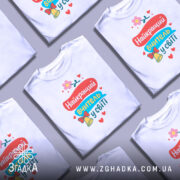 Футболка найкращий вчитель, біла, зображена на манекені, фон світло-сірий, принт містить яскраві кольори: червоний, блакитний, жовтий, з квіткою та дзвоником.