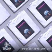 Футболка нам є куди дивитись. Біла футболка з принтом, на якому зображені дві фігури, що сидять на лавці під величезною землею на фоні зоряного неба. Принт має яскраві кольори, текст виконаний у неоновому стилі.